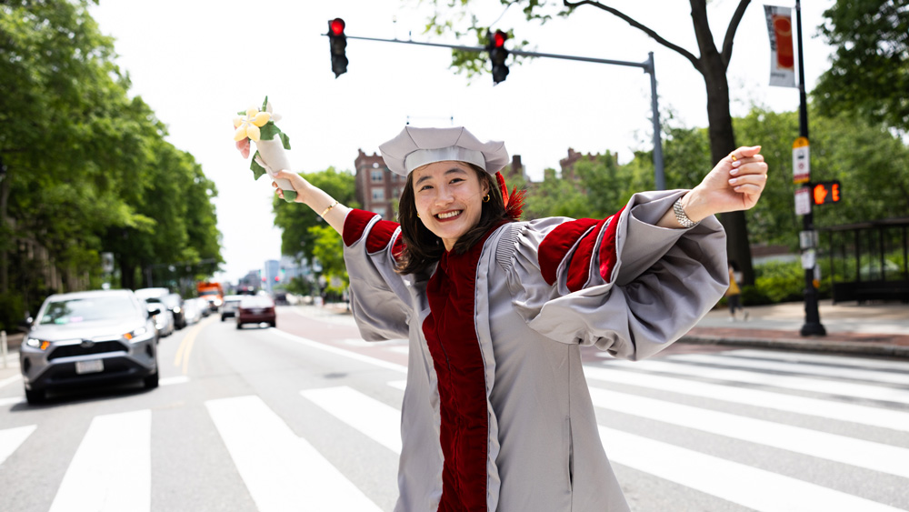 A graduate celebrating as she crosses 77 Massachusetts Ave in front of MIT