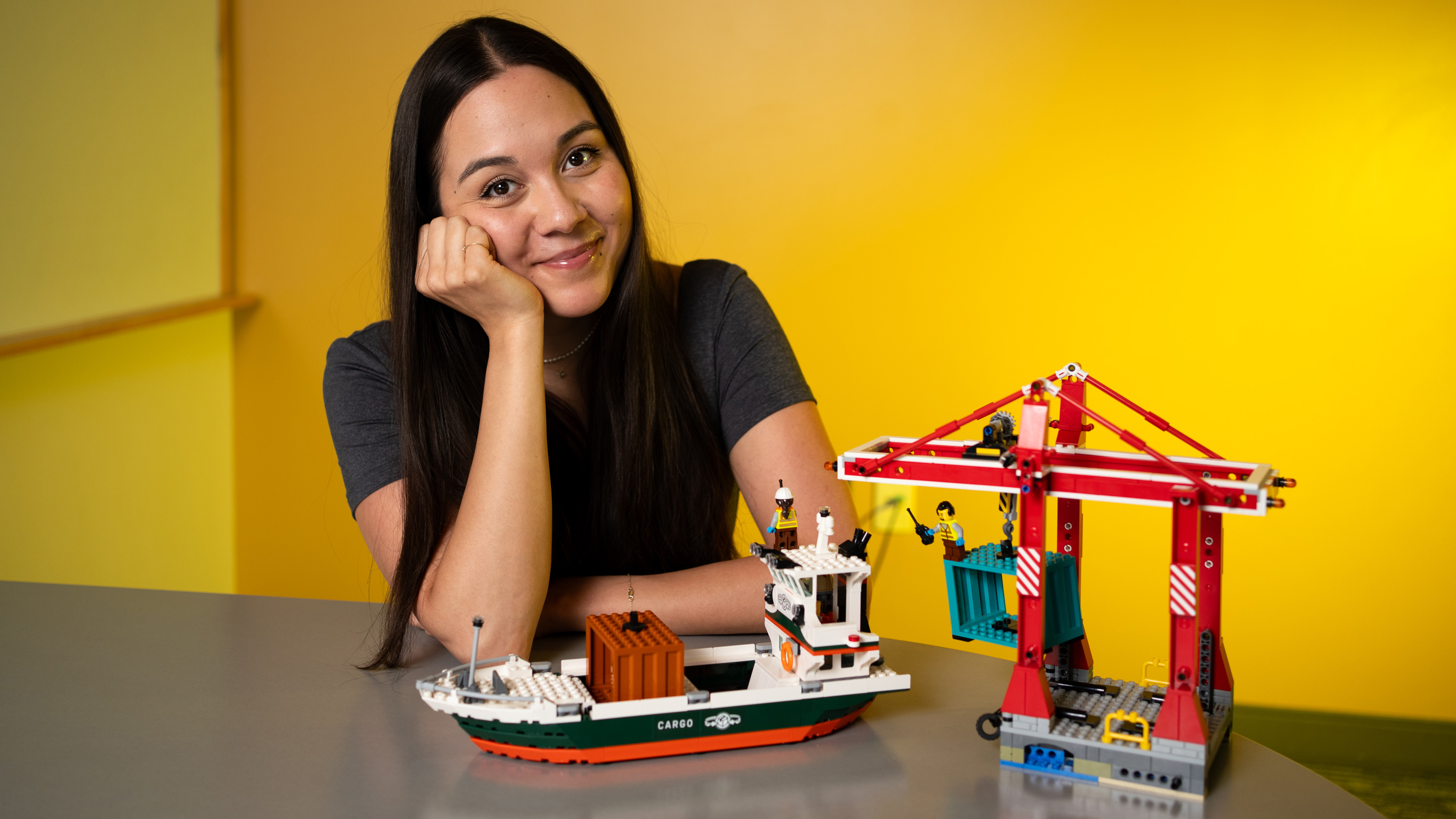 Chelsea Mitchell sits next to a Lego set of a shipping dock, with a crane and a boat