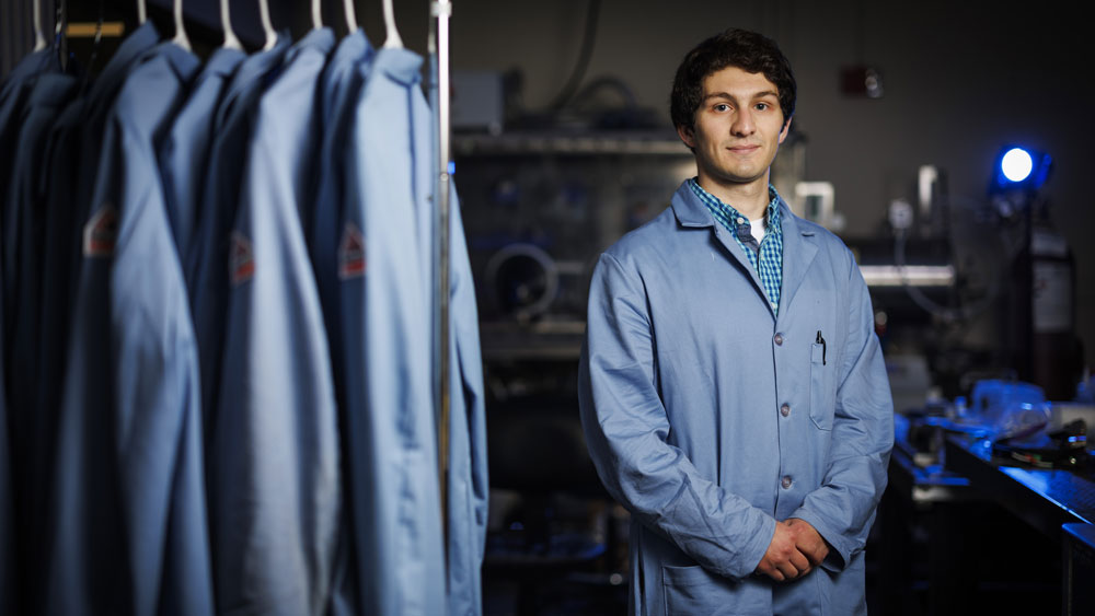Hugh Smith in lab next to lab coat rack