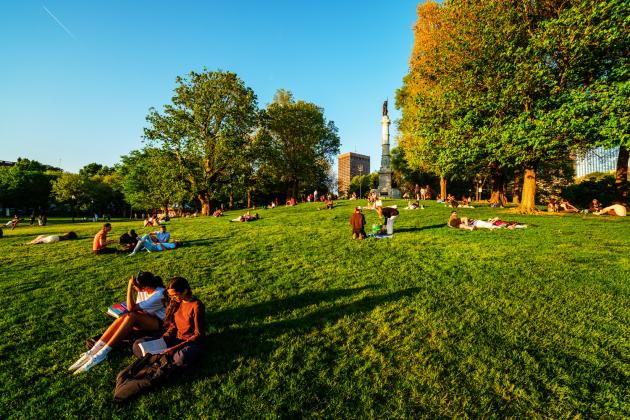 People relax on the Boston Common lawn beneath the Soldiers and Sailors Monument.