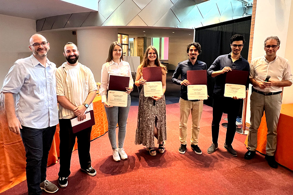 Seven people in a row, the second through fifth are holding award certificates, third and fourth are women, others are men, MIT