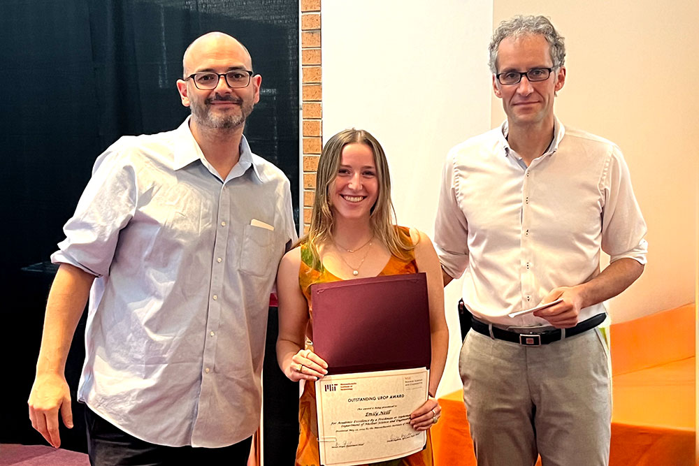Emily Neill in the center holding an award certificte with Matteo Buccito the left and Jacopo Buongiorno to the right, in a row, MIT