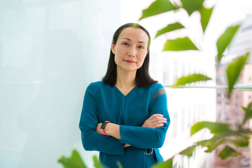 Haruko Wainwright portrait with arms crossed against a bright white background, with blurry plant leaves in foreground