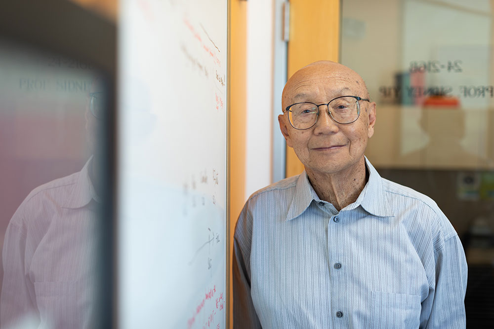 bespectacled male faculty member leaning against a whiteboard, MIT