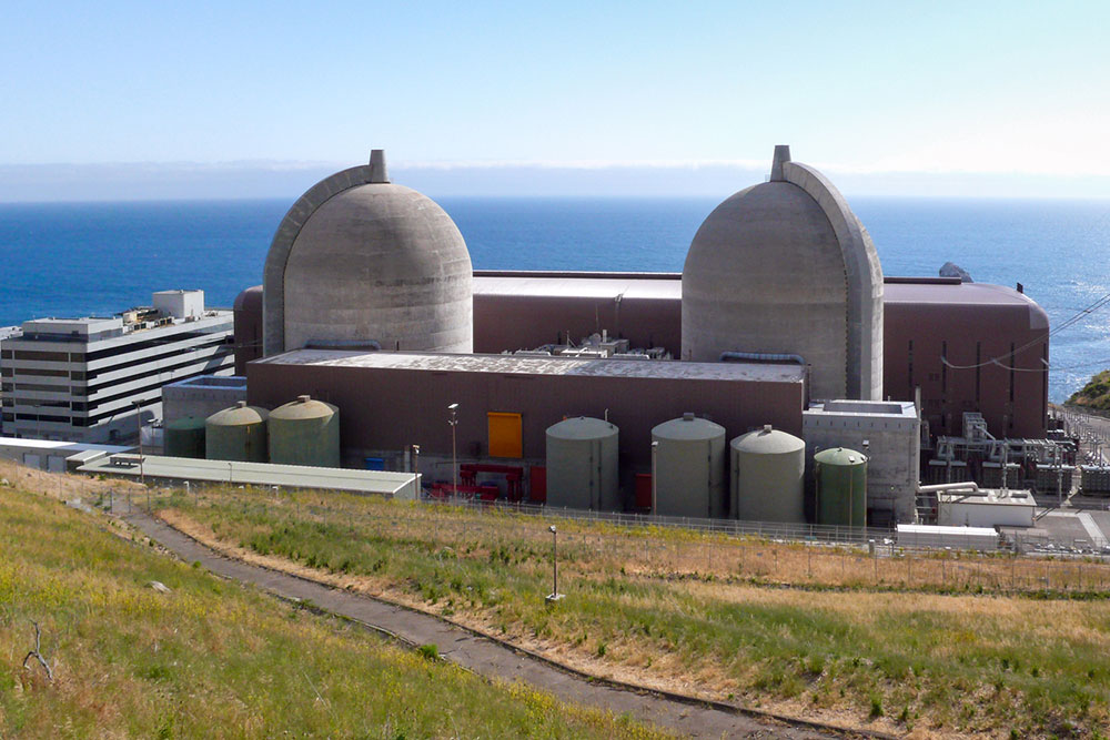 Diablo Canyon nuclear powerplant, cooling towers and cluster of buildings that make up the facility, with blue sky and ocean in the background and grass in the forground