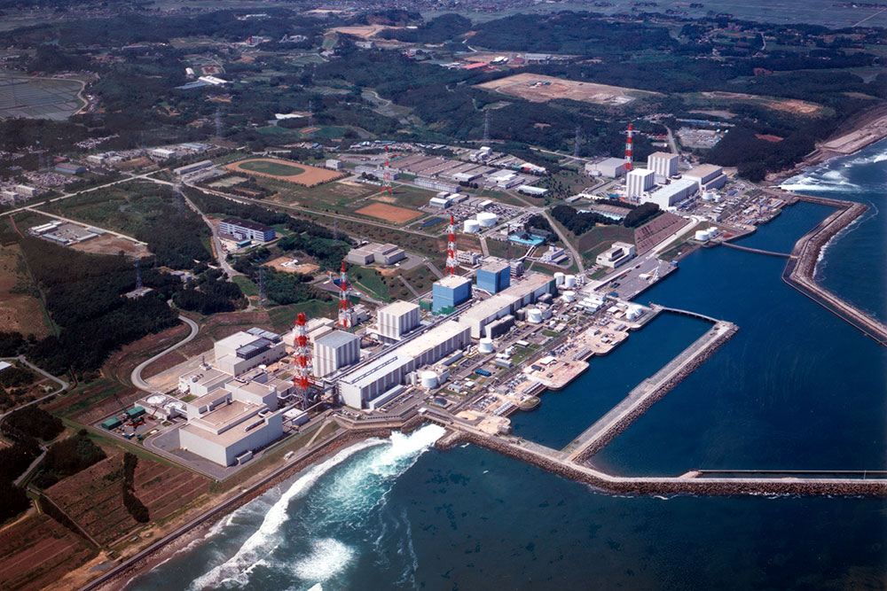Aerial photo of Fukushima Daichi Nuclear Power Station showing nuclear reactors and support systems, sited on the coastline, ocean in the foreground and to the right land in the background and to the left.