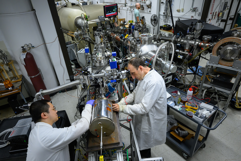 Associate Professor Michael Short on the right and postdoc Dr. Weiyue Zhou on the let working on a test chamber containing a metal in a lab with large instuments