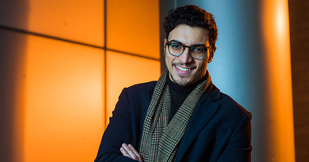 Male grad student standing against an orange background, MIT